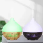 Difusores de aceites esenciales con luz LED: uno con base de madera y luz verde, y otro con base negra y luz morada, ambos emitiendo vapor.