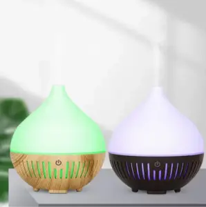 Difusores de aceites esenciales con luz LED: uno con base de madera y luz verde, y otro con base negra y luz morada, ambos emitiendo vapor.