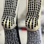 Dos medias antideslizantes deportivas para fútbol, una negra y otra blanca, con suela adherente de tacos negros texturizados para mayor estabilidad.