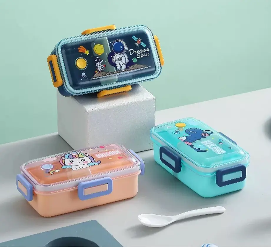 Tres fiambreras infantiles rectangulares con tapa transparente y cierres laterales, diseños de astronauta, unicornio y dinosaurio, incluyen cuchara blanca.