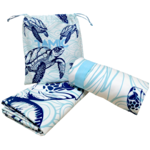 Toalla de microfibra azul con tortugas marinas, enrollada junto a una doblada y su bolsa con cordón para viajes.