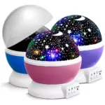 Tres proyectores de estrellas LED con base blanca y cúpula en colores azul, rosa y morado, uno con cubierta semitransparente removida.