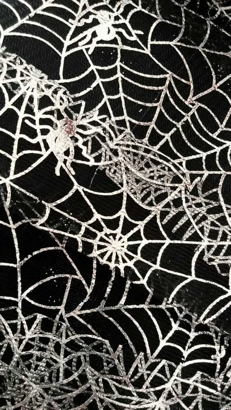 Tela negra de disfraz para niñas con diseño estampado de telarañas plateadas brillantes y pequeñas arañas blancas.