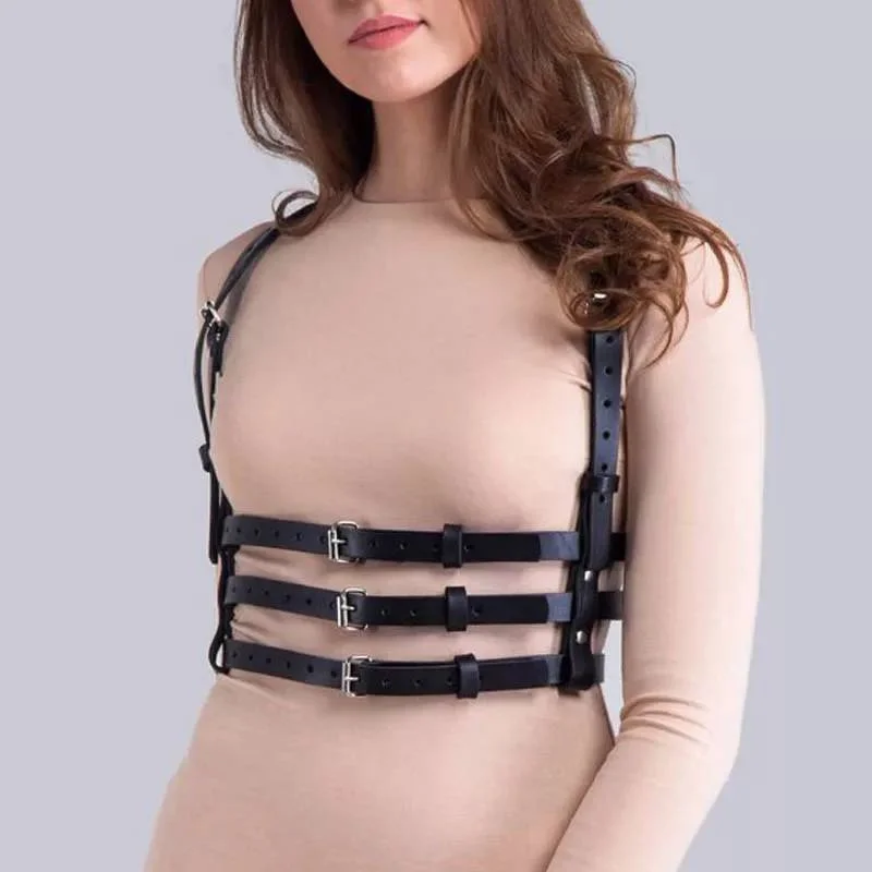 Arnés de cuero negro ajustable con tres correas horizontales en el pecho, sobre blusa beige de manga larga.