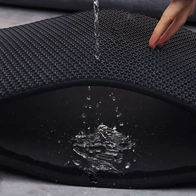 Tapete arenero para gato doble capa de goma EVA negra, mostrando su interior impermeable mientras cae agua.