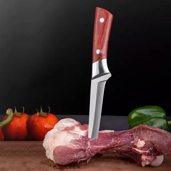 Cuchillo de cocina con hoja de acero inoxidable y mango ergonómico de madera roja, clavado en un corte de carne cruda sobre tabla, junto a tomates y pimentón.