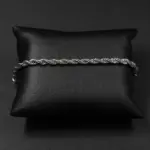 Pulsera de cadena estilo cuerda en acero inoxidable plateado, dispuesta horizontalmente sobre un cojín de cuero sintético negro.