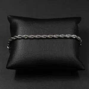 Pulsera de cadena estilo cuerda en acero inoxidable plateado, dispuesta horizontalmente sobre un cojín de cuero sintético negro.