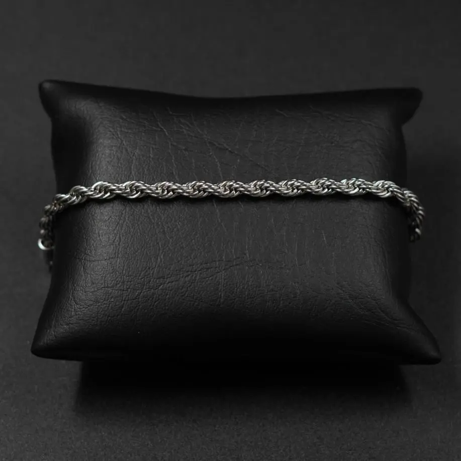 Pulsera de cadena estilo cuerda en acero inoxidable plateado, dispuesta horizontalmente sobre un cojín de cuero sintético negro.
