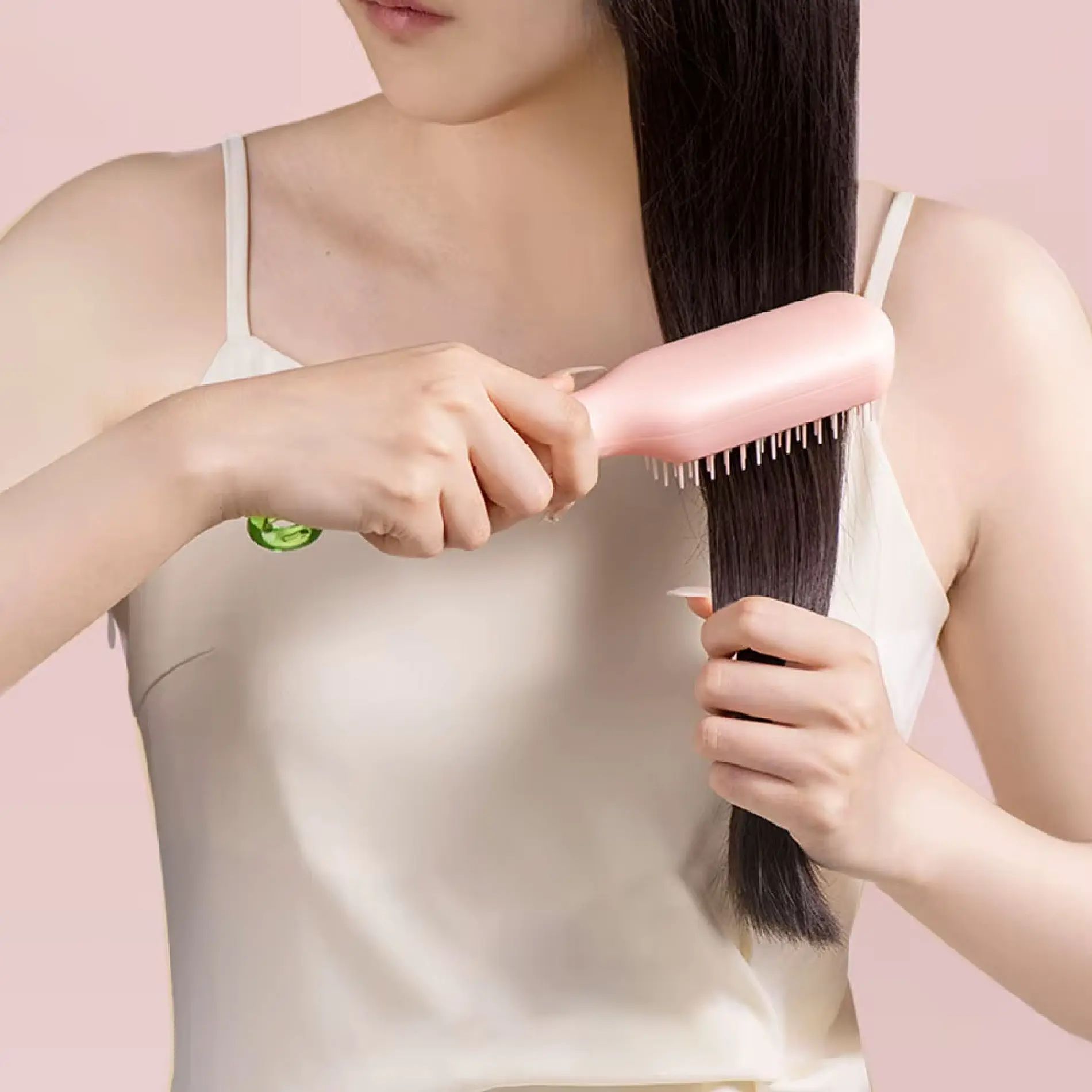 Mujer cepillando su cabello liso con un cepillo retráctil autolimpiante de color rosa, sosteniendo un mechón con la otra mano.
