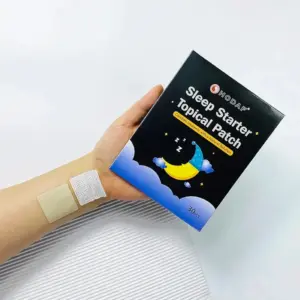 Mano sosteniendo caja negra de parches para dormir junto a un parche beige aplicado en el brazo y su protector blanco.