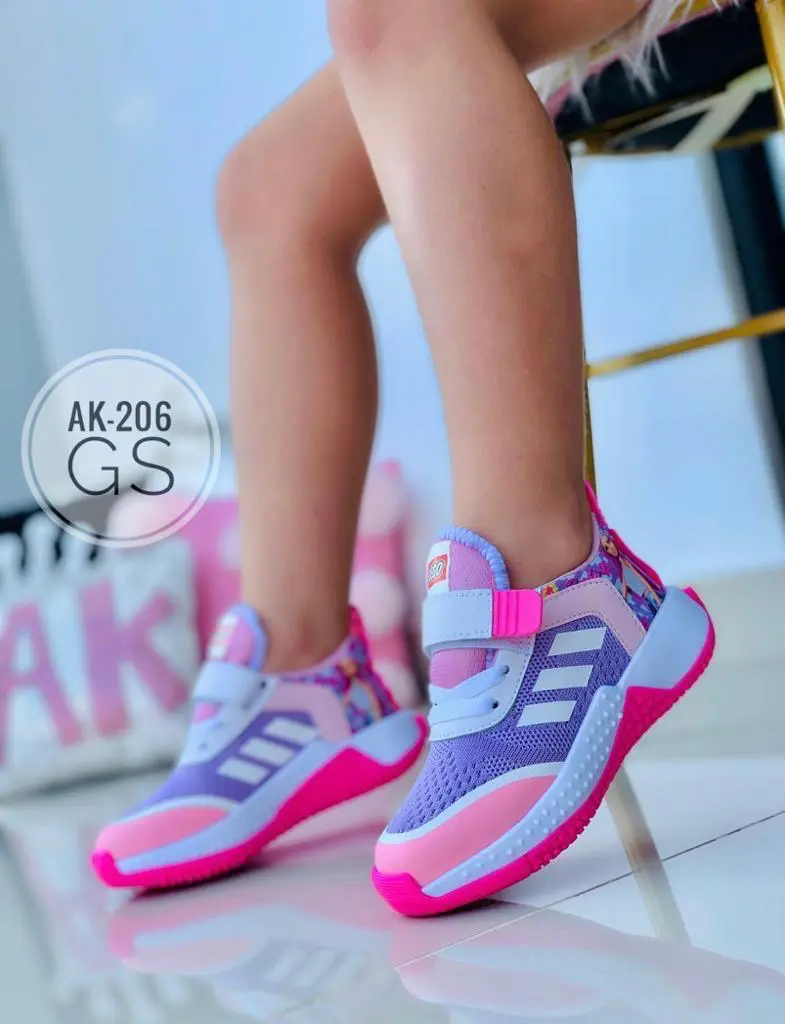 Zapatillas deportivas infantiles en tonos morado, rosa y azul con rayas blancas, cierre de velcro y suela rosa, vistas de perfil en un niño.