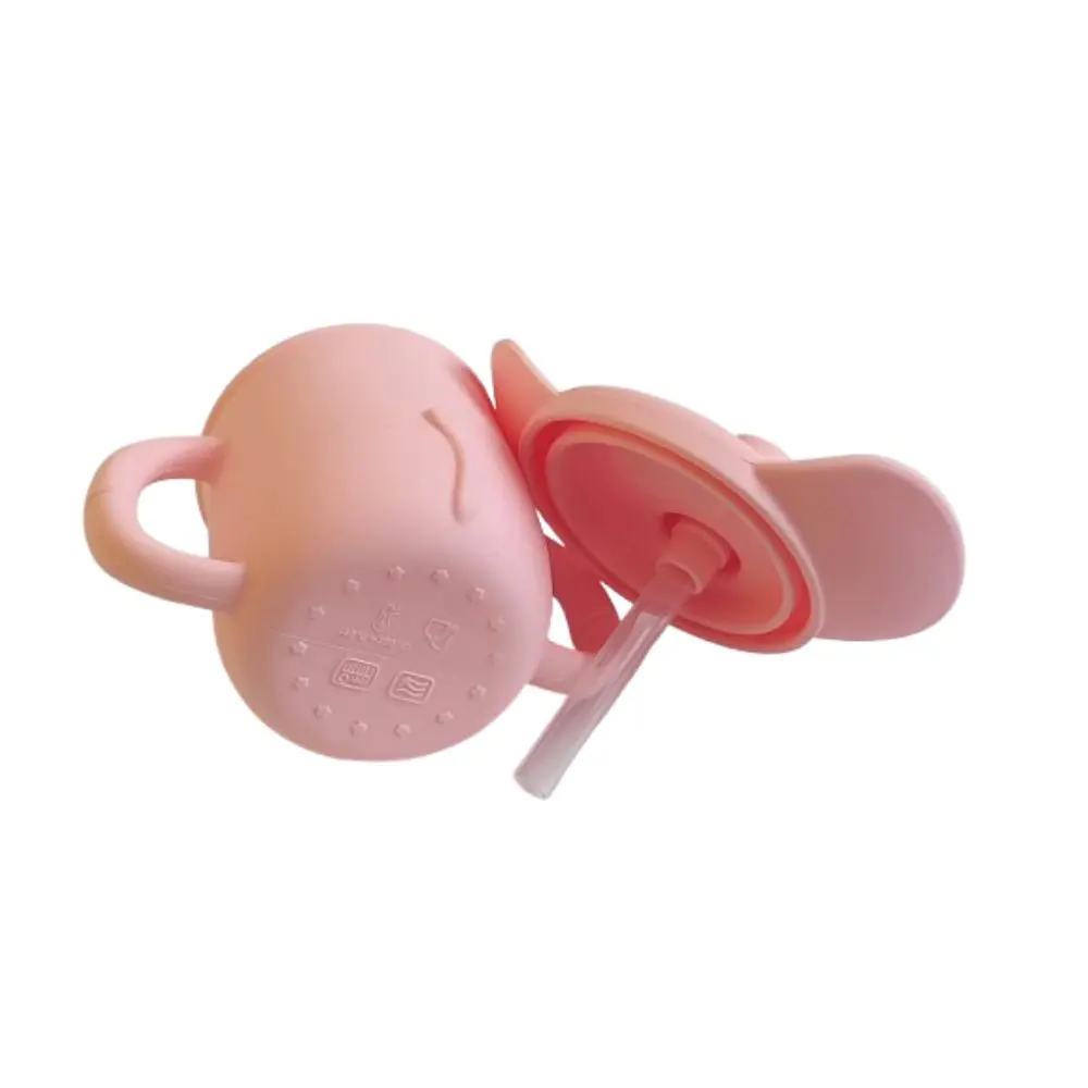 Vaso de aprendizaje de silicona rosa con diseño de elefante, dos asas y tapa con orejas decorativas y pitillo transparente.