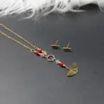 Set de collar corbatín y aretes dorados con cuentas de murano rojas y dije de media luna grabada.