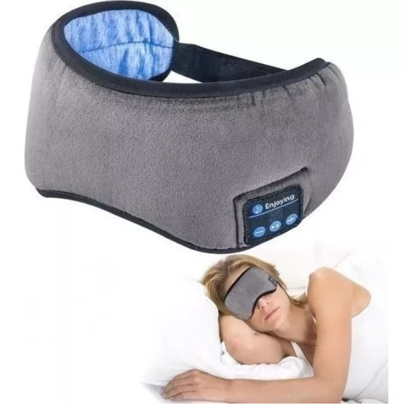 Antifaz de descanso gris con audífonos inalámbricos integrados y panel de control, mostrado en uso sobre una mujer acostada en una cama.