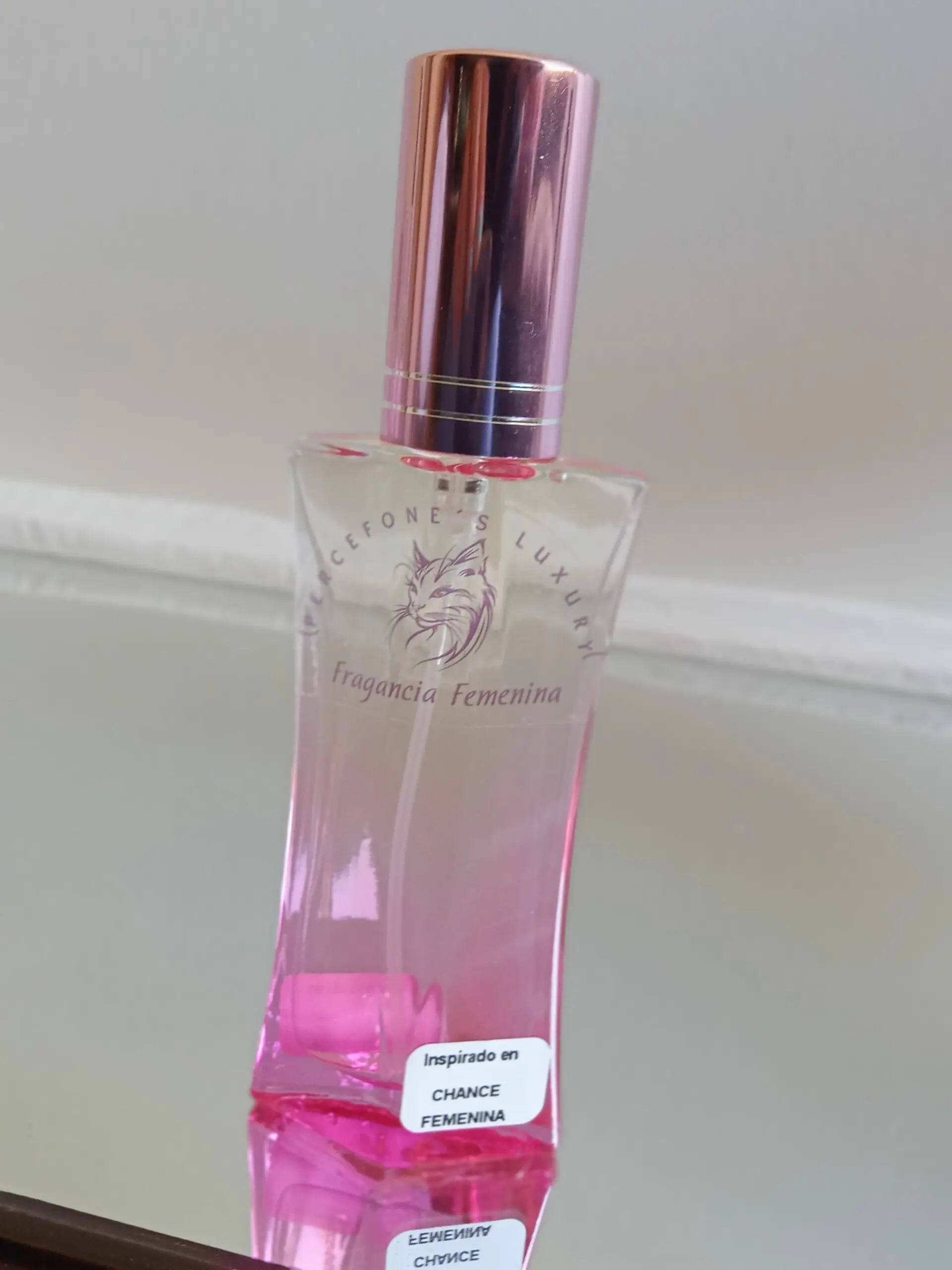 Frasco de vidrio de 30ml con líquido rosado, tapa metálica oro rosa e inspiración en Chance Femenina, sobre superficie reflectante.