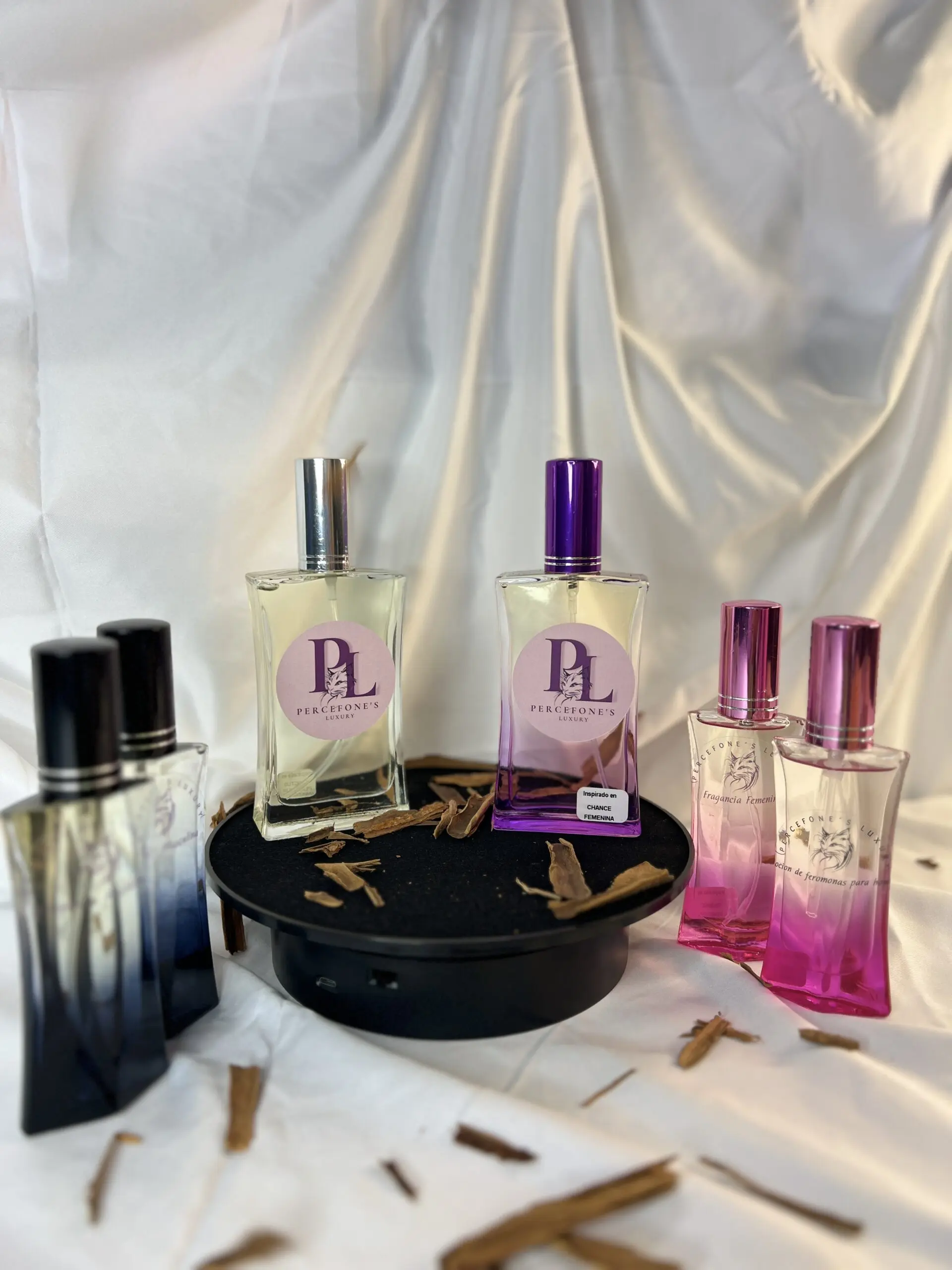 Variedad de fragancias femeninas de 30ml en frascos de vidrio con tonos azul, transparente y rosa sobre una base negra y tela blanca.
