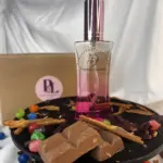 Fragancia femenina Chance X1 de 30ml con degradado rosado, rodeada de chocolate, canela y gomitas de colores sobre una base negra.