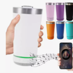 Vaso térmico blanco con altavoz Bluetooth en la base, sostenido por una mano, junto a una muestra de colores disponibles y un celular reproduciendo música.