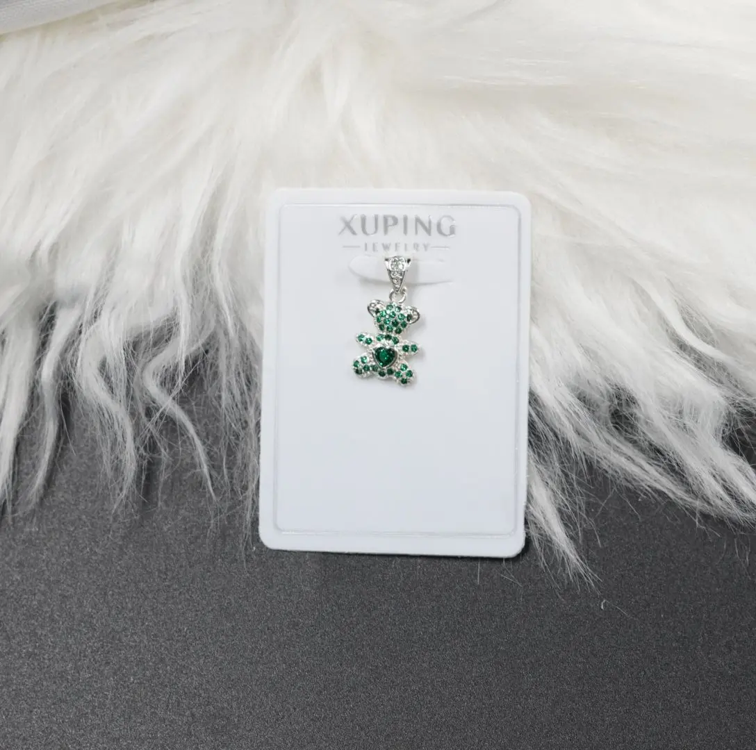 Colgante plateado en forma de oso cubierto de brillantes piedras verdes, exhibido sobre tarjeta blanca Xuping Jewelry junto a pelaje sintético.