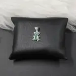 Colgante plateado en forma de oso con incrustaciones de piedras verdes y corazón central, sobre cojín negro.