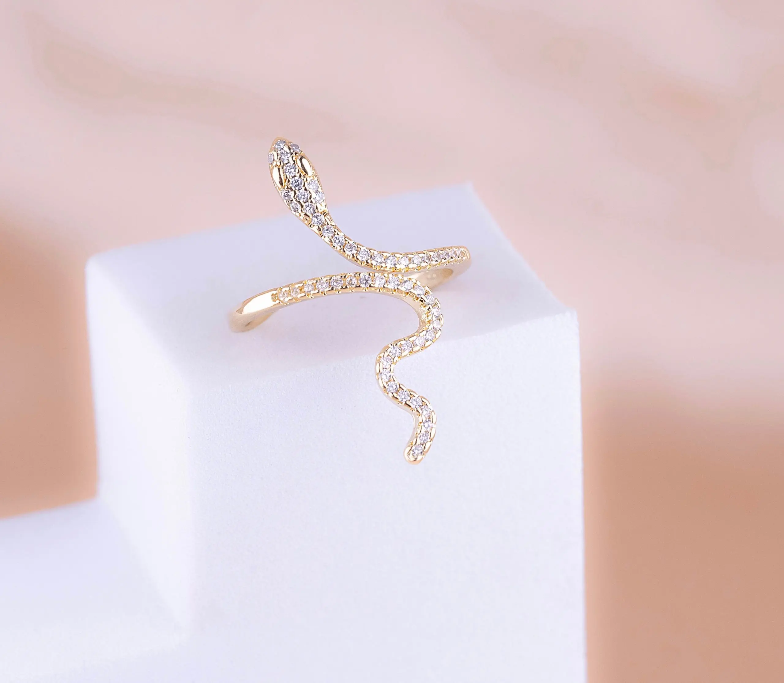 Anillo ajustable de serpiente en cover gold con micro circones brillantes, exhibido sobre una base blanca.