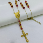 Camándula de baño de oro con cuentas de murano rojo, argollas doradas, medalla ovalada y crucifijo sobre fondo blanco.