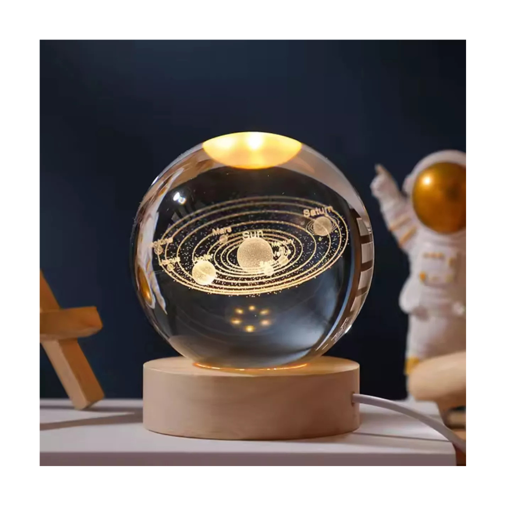 Lámpara esférica de cristal con grabado láser 3D del sistema solar, sobre base circular de madera iluminada, situada junto a figura de astronauta.