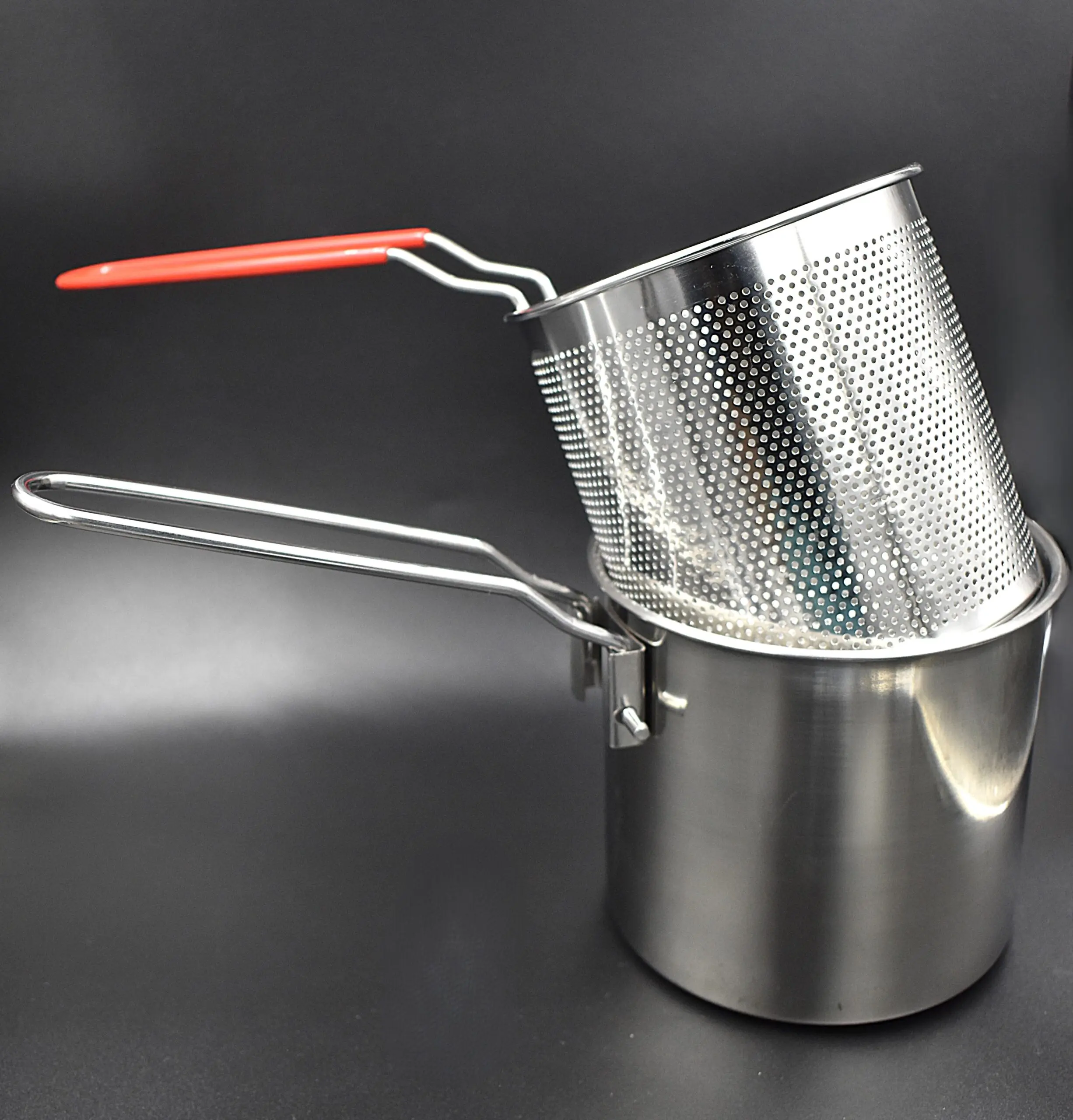 Olla freidora con cesta perforada de acero inoxidable, con mango de silicona roja, apoyada sobre fondo oscuro.