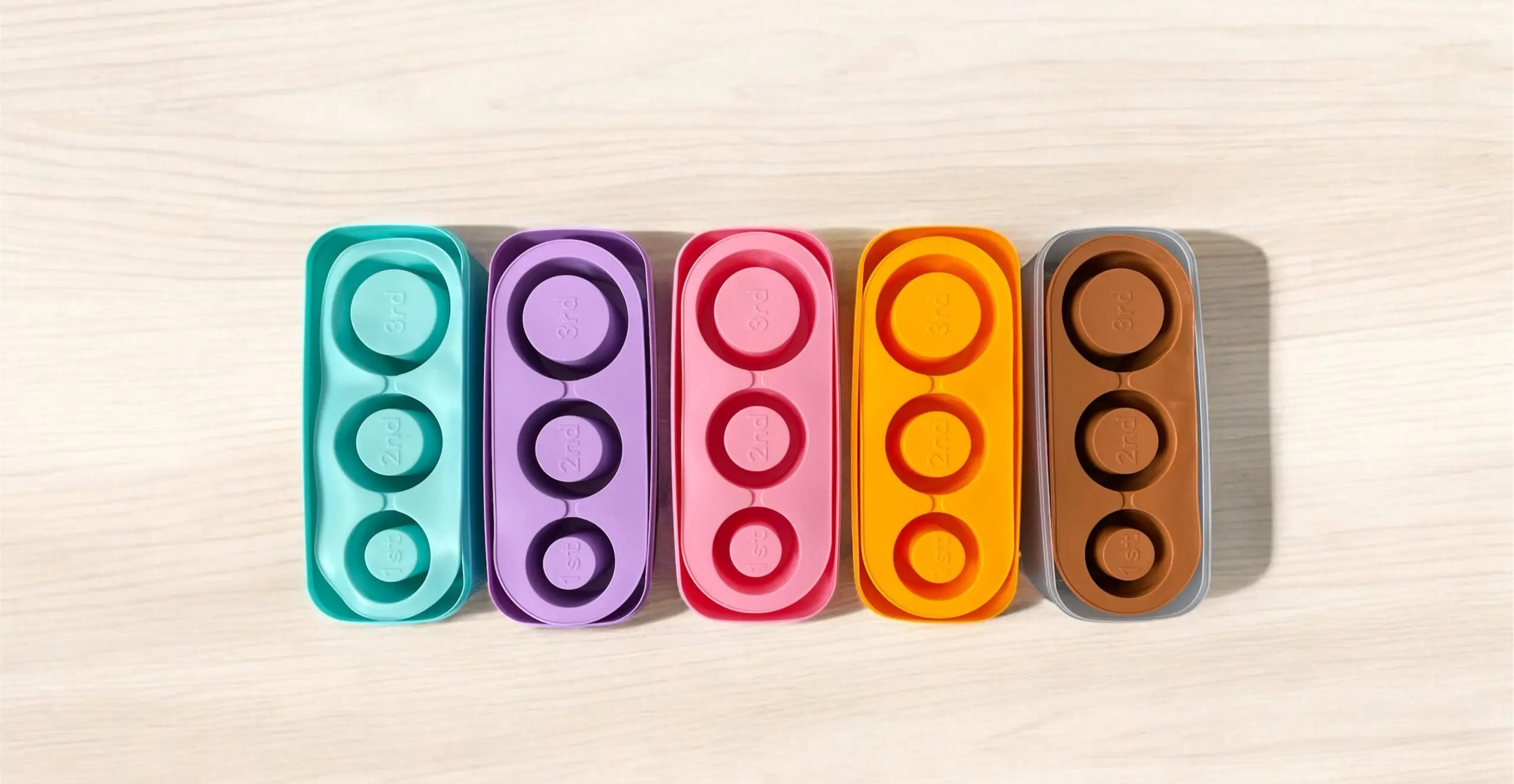 Set de dos moldes de silicona para hielo cilíndrico hueco Stanley en colores turquesa, morado, rosado, naranja y marrón sobre superficie clara.