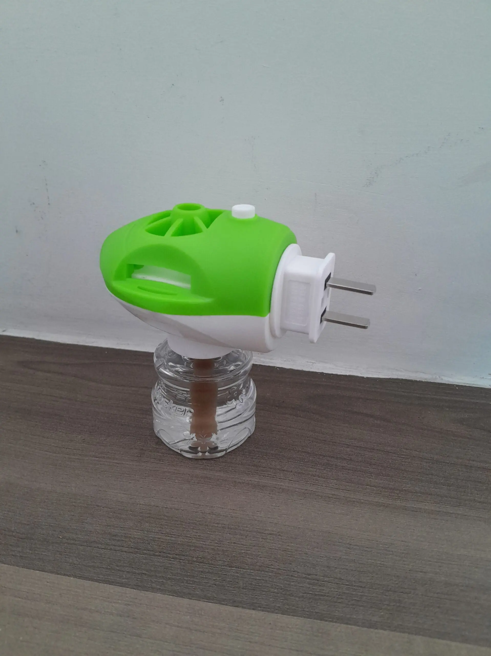 Repelente eléctrico para zancudos con carcasa verde y blanca, frasco transparente con líquido y mecha, sobre superficie de madera oscura.