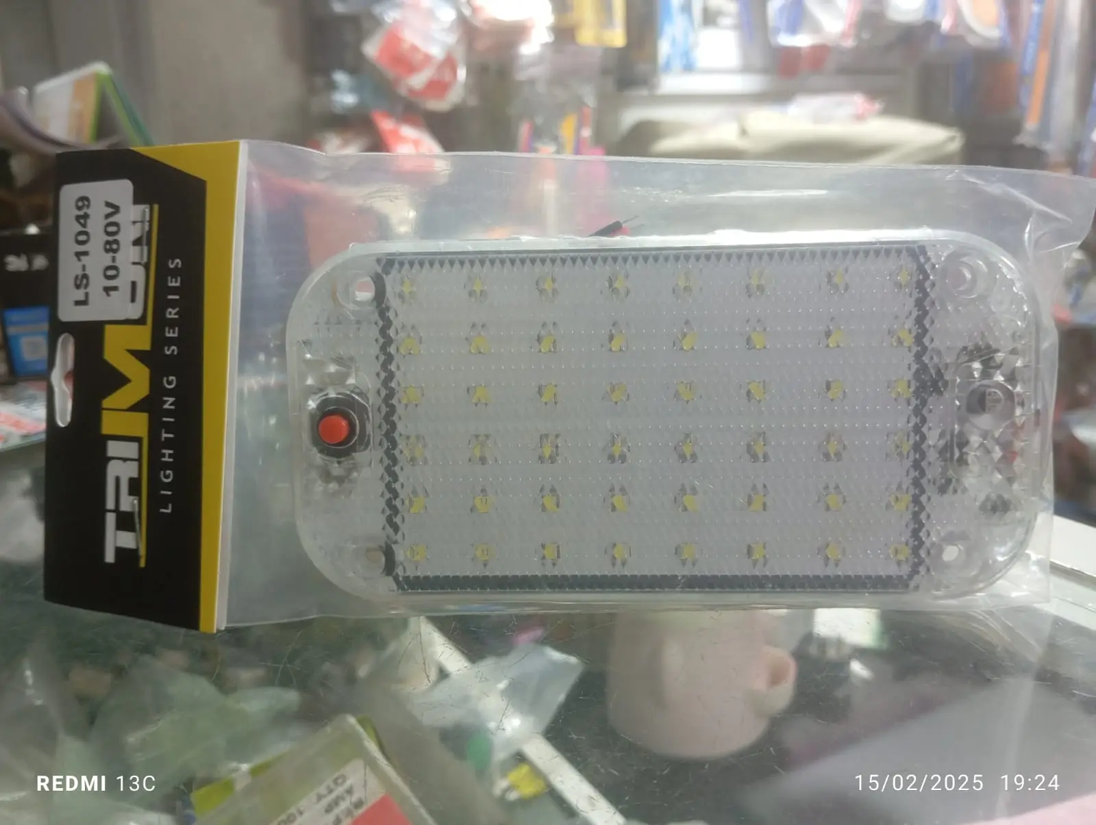 Plaqueta de techo LED rectangular Trim 10-80V con interruptor rojo en bolsa plástica transparente sobre superficie de vidrio.