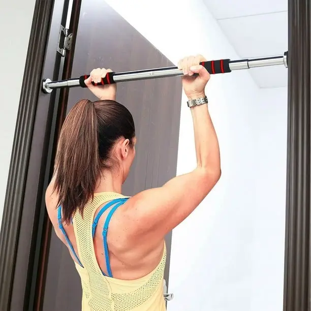 Barra de ejercicio metálica con agarres negros y rojos instalada en un marco de puerta, usada para entrenamiento de espalda y brazos.
