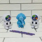 Set de dos sacapuntas manuales diseño astronauta en blanco y uno azul al centro con palanca y dos lápices morados sobre fondo de ladrillo blanco.