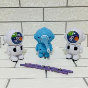 Set de dos sacapuntas manuales diseño astronauta en blanco y uno azul al centro con palanca y dos lápices morados sobre fondo de ladrillo blanco.