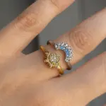 Set de dos anillos ajustables: uno dorado con diseño de sol y otro plateado con forma de luna creciente decorada con piedras blancas y azules.