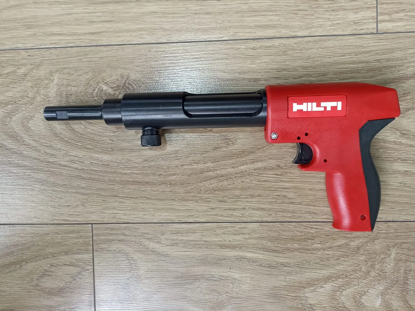 Pistola de fijación Hilti DX 30 roja y negra sobre piso de madera, herramienta manual para construcción.