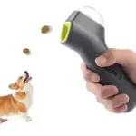 Lanzador de golosinas gris con boquilla verde lima disparando premios hacia un perro corgi, demostrando su uso para adiestramiento.
