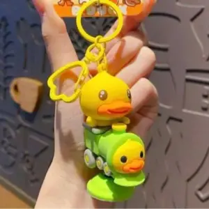 Llavero de silicona con pato amarillo sobre un tren verde y otro patito frontal, con aro y dije de flor amarillos.