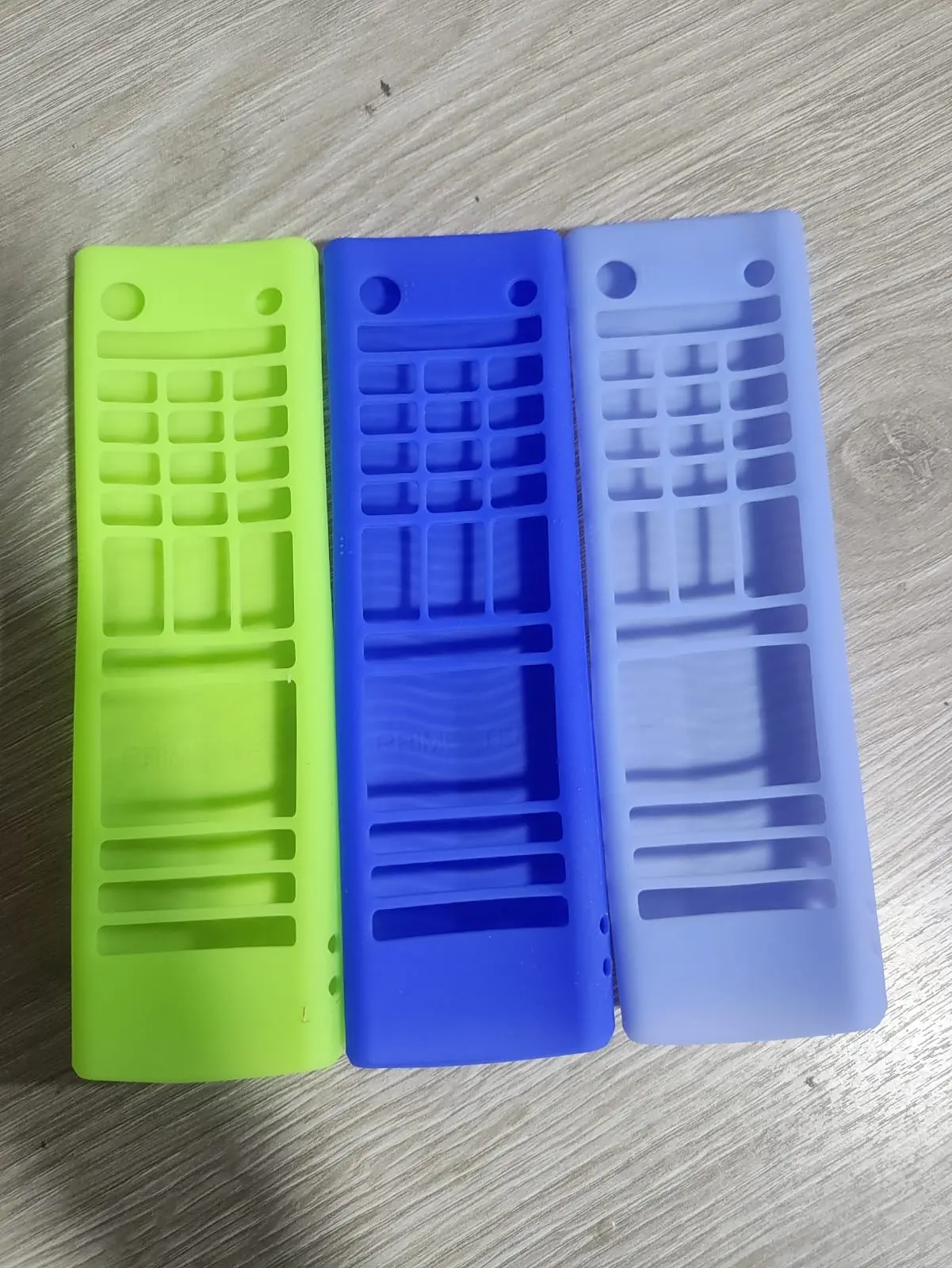 Tres fundas de silicona para control remoto LG clásico en colores verde claro, azul y lila, dispuestas sobre superficie de madera.