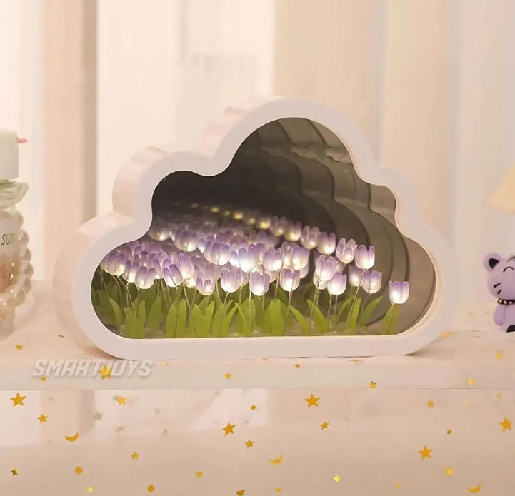 Lámpara espejo con marco blanco en forma de nube, tulipanes morados y luces LED cálidas, sobre una superficie decorada con estrellas doradas.