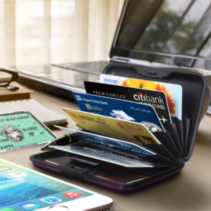 Cartera rígida negra con tarjetas de crédito desplegadas en abanico sobre un escritorio junto a un celular y una laptop.