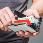Tarjetero de aluminio plateado con acordeón desplegable que contiene tarjetas bancarias, billetes y organizador interno visible.