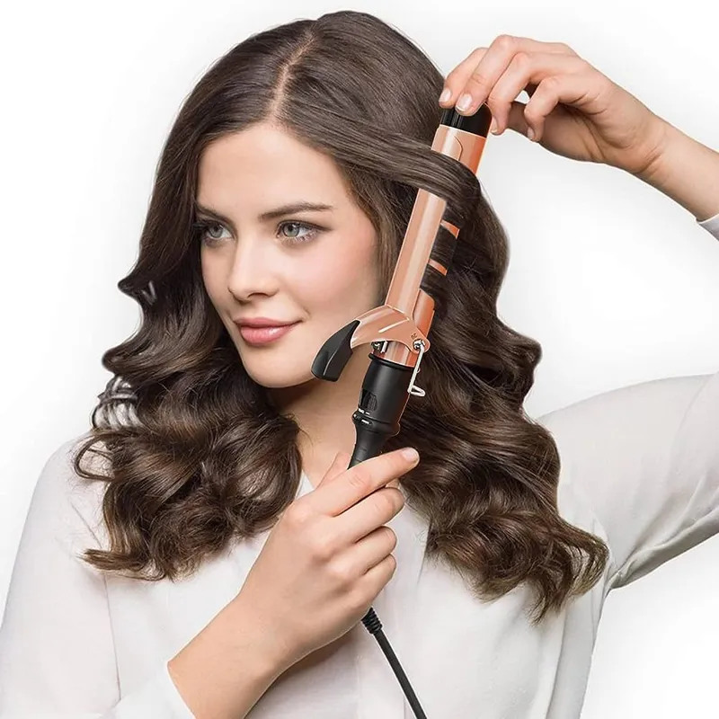 Mujer usando pinza rizadora de cerámica color oro rosa y negro para definir ondas en cabello castaño largo.