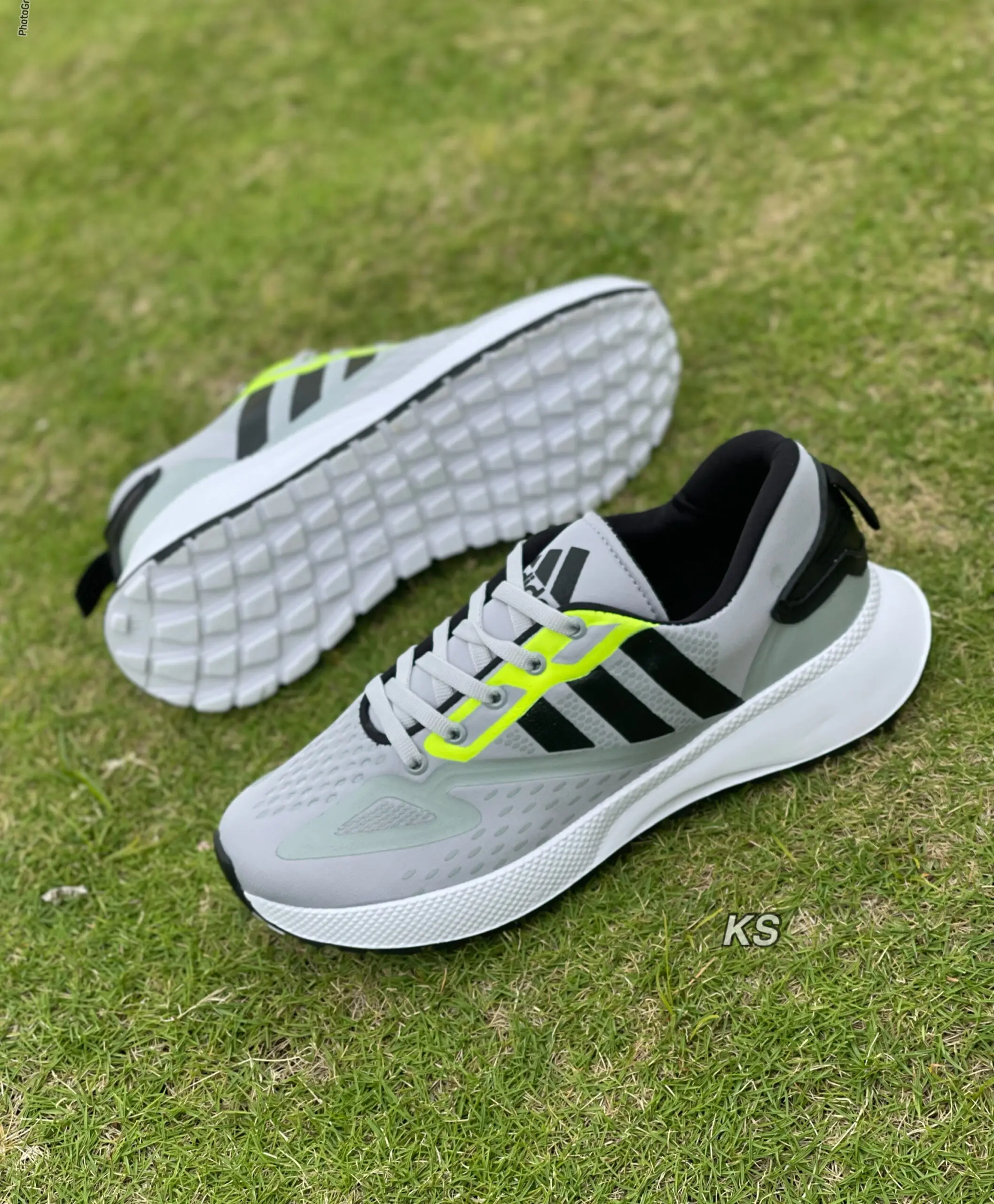 Tenis deportivos para hombre grises con negro, detalles en amarillo neón, suela blanca flexible y capellada perforada sobre césped.