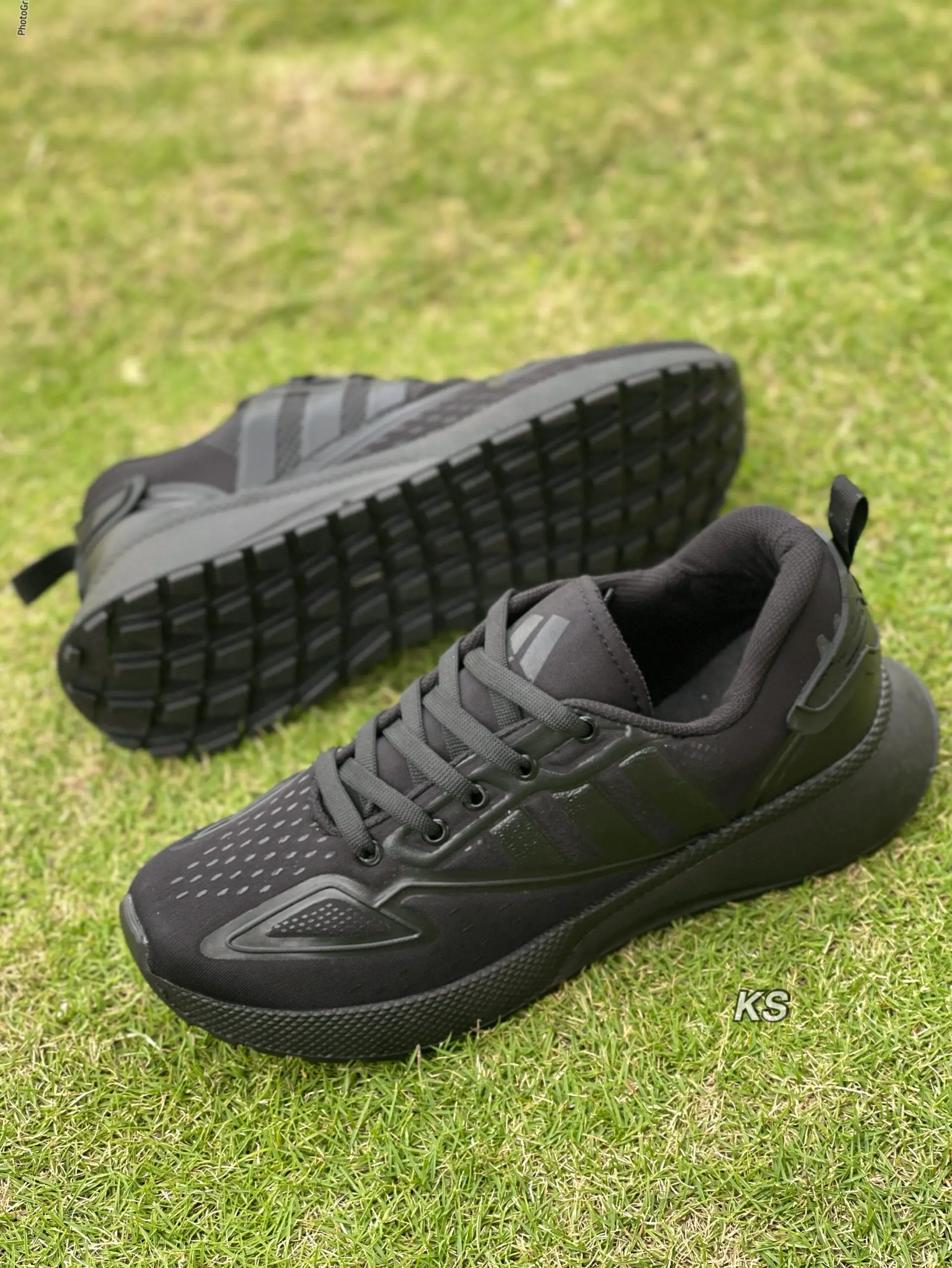 Zapatillas deportivas negras para hombre con suela dentada flexible, colocadas sobre césped verde, mostrando lateral y suela.