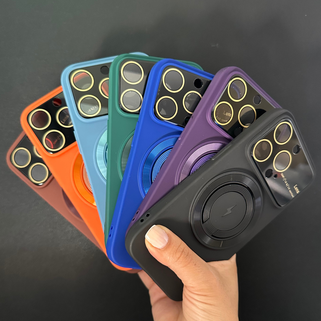 Mano sosteniendo funda MagSafe negra con protector de lentes integrada, desplegando en abanico opciones en colores morado, azul, verde, naranja y marrón.