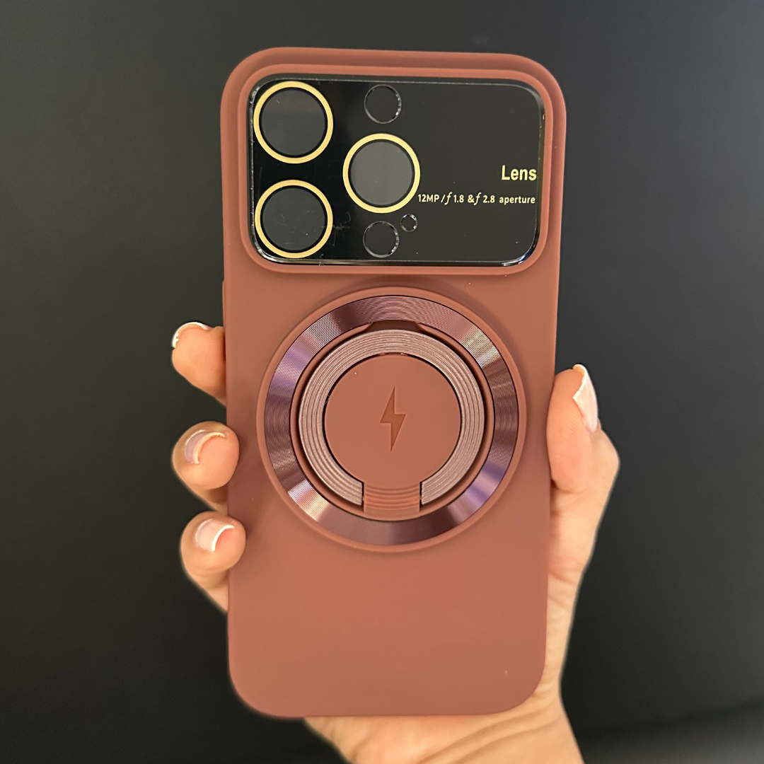 Funda de silicona color terracota con protector de lentes y anillo MagSafe con símbolo de rayo, sostenida por una mano.