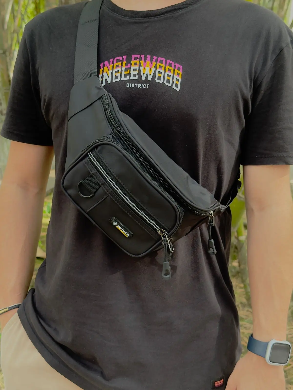 Riñonera urbana negra para hombre con múltiples compartimentos y cremalleras, usada de forma cruzada sobre el pecho en un estilo casual.