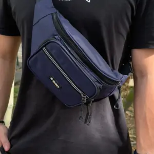 Riñonera azul oscuro de hombre con correa ajustable negra, diseño urbano cruzado sobre el pecho, bolsillos múltiples con cremallera y parche frontal.